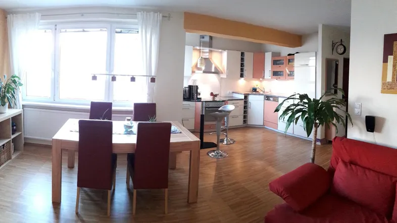 Helles Wohn- und Esszimmer mit offener Küche, Parkettboden und großen Fenstern.