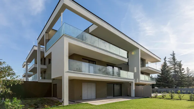 Modernes Mehrfamilienhaus mit großen Balkonen, Glasgeländern und gepflegter Rasenfläche.