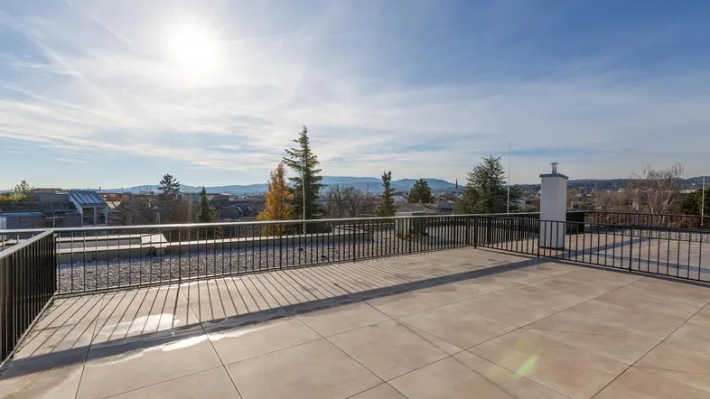 Große Dachterrasse mit Fliesenboden, schwarzem Geländer und weitem Blick über die Stadt und Berge.