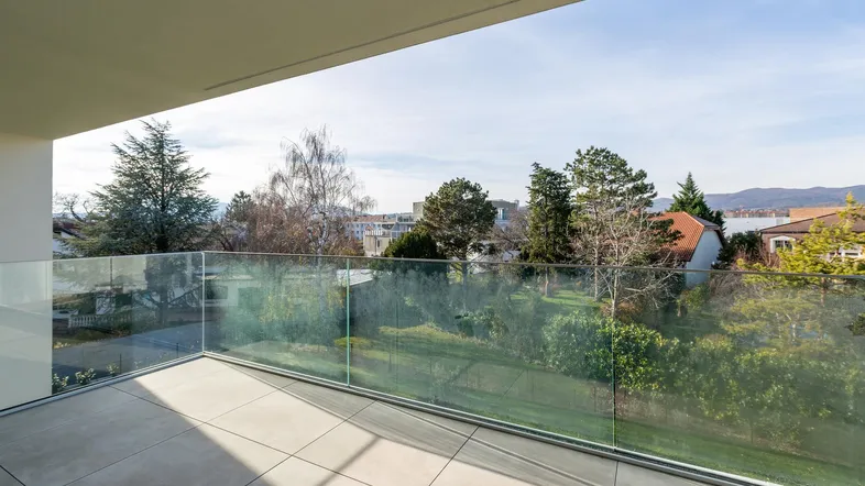 Heller Balkon mit Glasgeländer und Fliesenboden bietet einen weiten Blick ins Grüne.