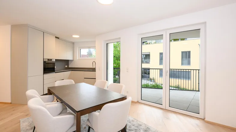 Moderner offener Wohn-Essbereich mit integrierter Küche, Holzboden und Zugang zum Balkon.
