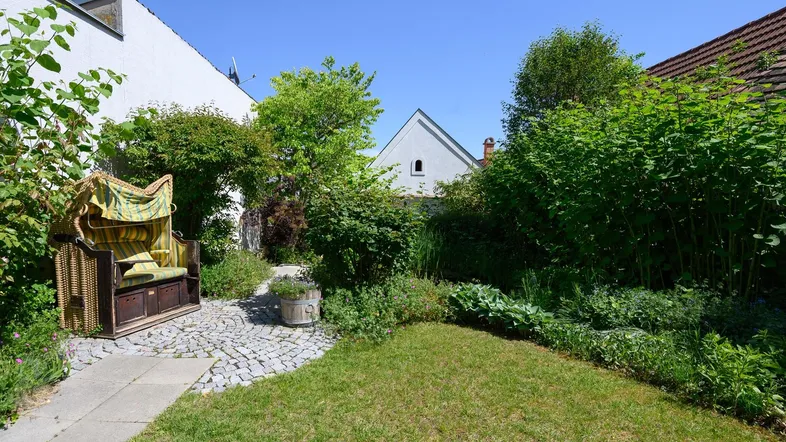 Gepflegter Gartenbereich mit Rasenfläche, üppiger Bepflanzung und einem Strandkorb zum Entspannen.