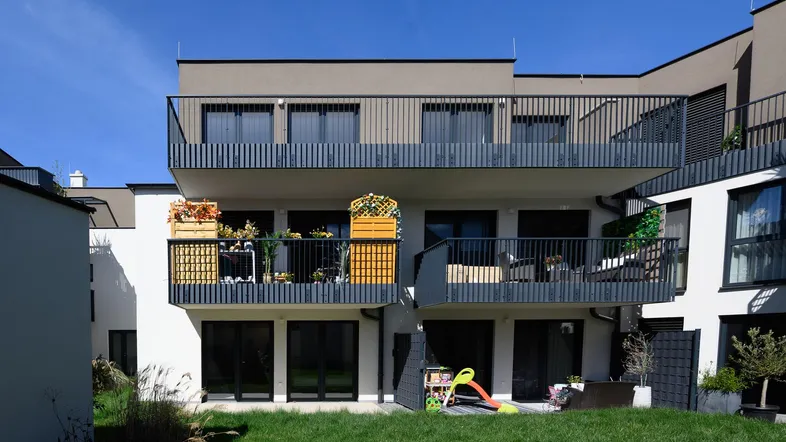 Moderne Wohnanlage mit mehreren Balkonen, dunklen Geländern und einem kleinen Rasenbereich.