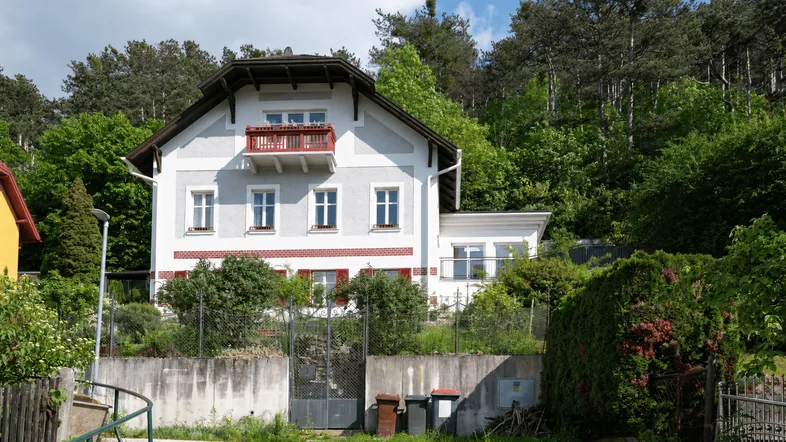Traditionelles Haus an einem Hang gelegen, umgeben von üppigem Grün und Bäumen.