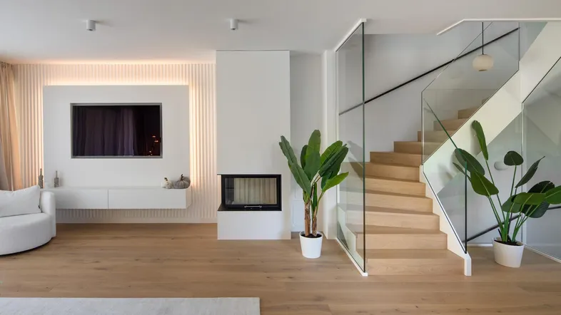 Modernes Wohnzimmer mit Kamin, Fernseher und offener Treppe, hell und geräumig gestaltet.