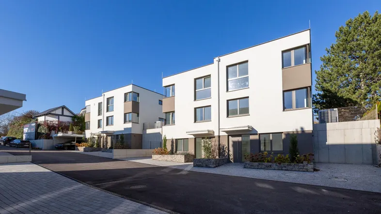 Moderne Reihenhäuser mit weißer Fassade und großen Fenstern unter blauem Himmel.