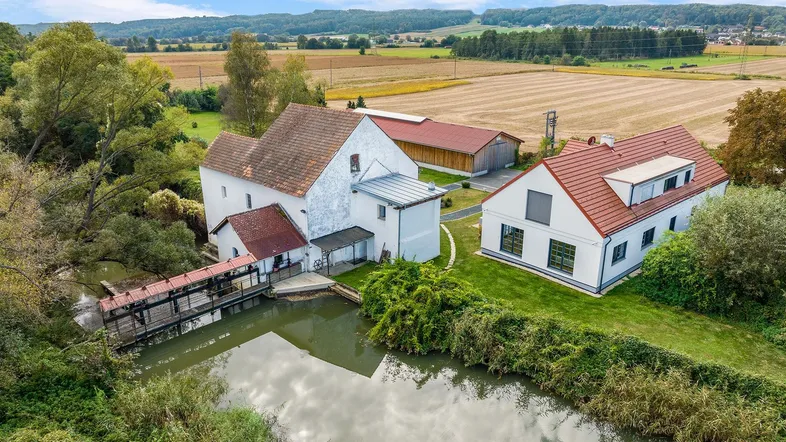 Luftaufnahme eines Anwesens mit zwei Gebäuden und einem Wasserlauf, umgeben von Feldern und Natur.