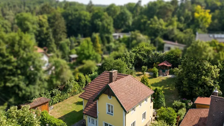 Luftaufnahme eines gelben Hauses mit rotem Dach, umgeben von viel Grün und Bäumen.