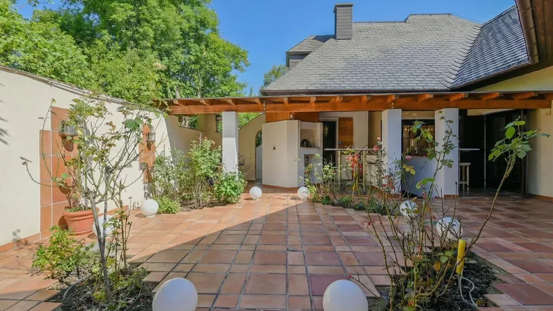 Große geflieste Terrasse mit Holzpergola, Pflanzen und Zugang zum Haus, ideal für Entspannung im Freien.