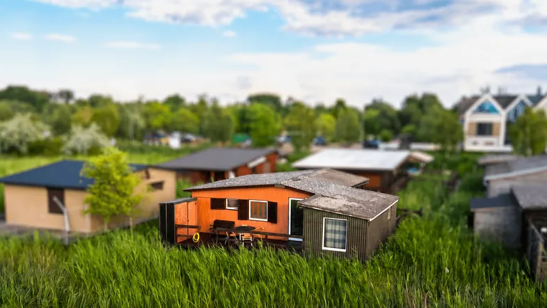 Luftaufnahme einer Ferienhaussiedlung mit kleinen Bungalows und viel Grünfläche unter blauem Himmel.