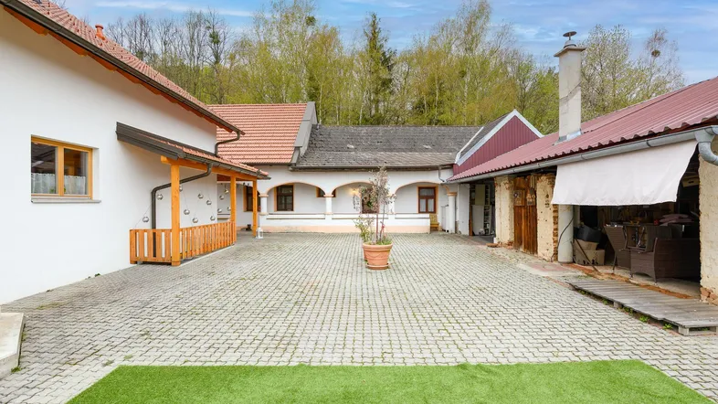 Gepflasterter Innenhof mit Grünfläche und mehreren Gebäuden, umgeben von Bäumen.