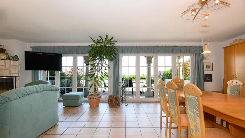 Geräumiger Wohn-Essbereich mit Fliesenboden, Kamin und Zugang zur Terrasse.