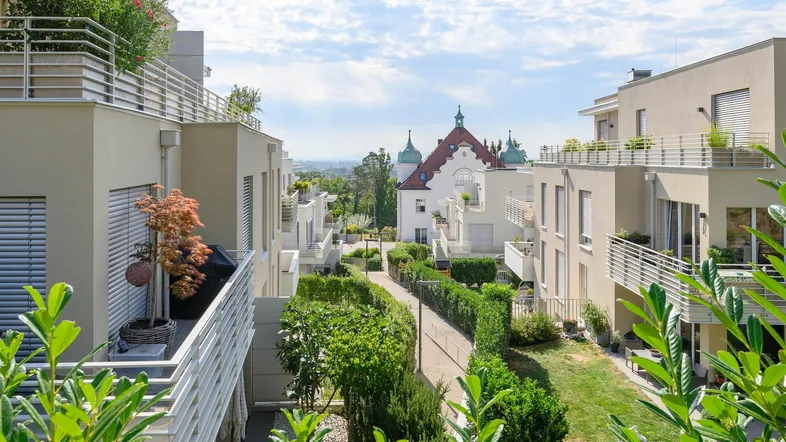 Blick auf eine moderne Wohnanlage mit begrünten Balkonen und einem historischen Gebäude im Hintergrund.
