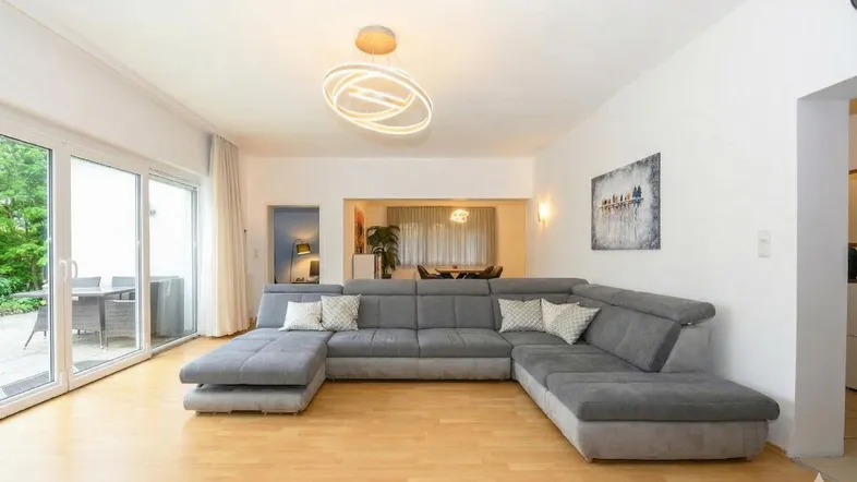 Helles Wohnzimmer mit großem Ecksofa, Holzboden und Zugang zur Terrasse.