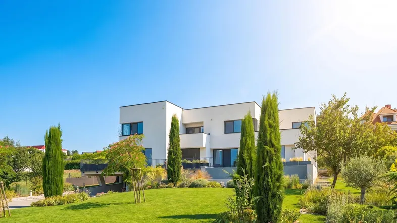 Moderne Wohnanlage mit gepflegtem Garten und Zypressen unter strahlend blauem Himmel.