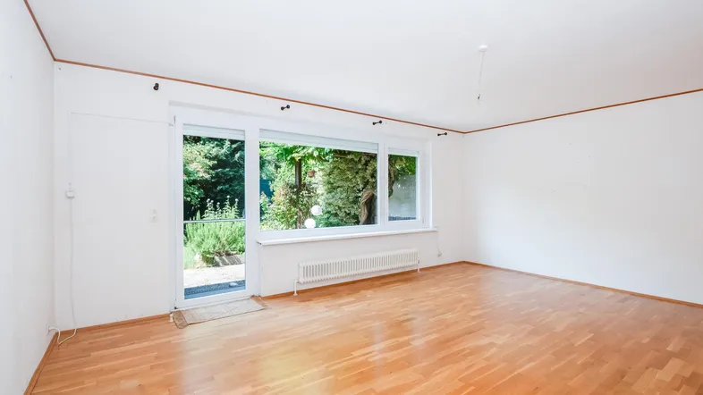 Helles Wohnzimmer mit Parkettboden und Zugang zum Garten, umgeben von viel Grün.
