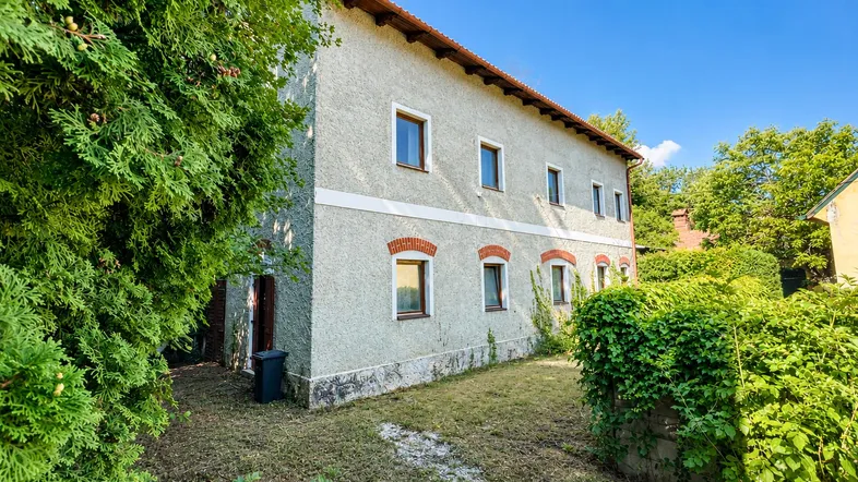 Das Gebäude zeigt eine schlichte Fassade mit kleinen Fenstern und einem grünen Gartenbereich.