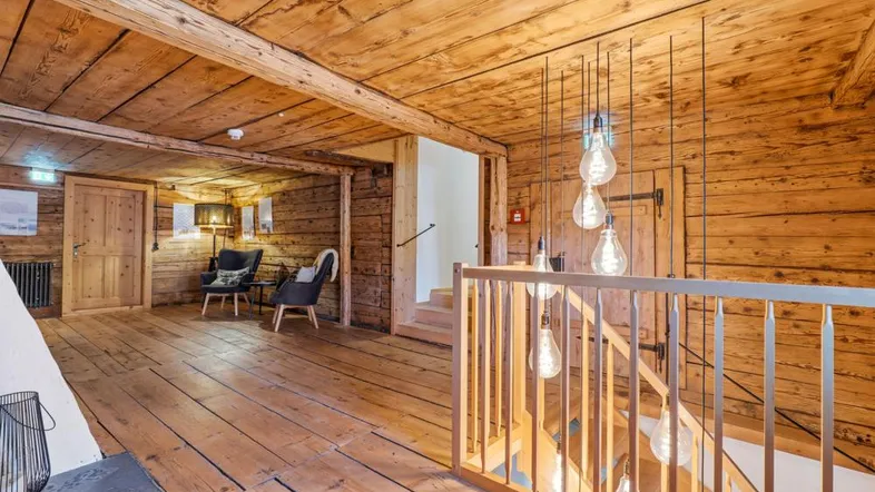 Geräumiger Flur mit rustikalen Holzvertäfelungen, Holzbalken und einer modernen Hängelampe über der Treppe.