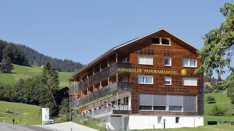 Traditionelles Holzhotel in den Bergen mit Balkonen und Blick auf die grüne Landschaft.