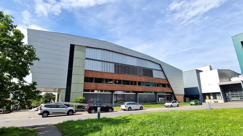 Moderne Gebäudefassade mit großen Fenstern und umliegenden Grünflächen unter blauem Himmel.