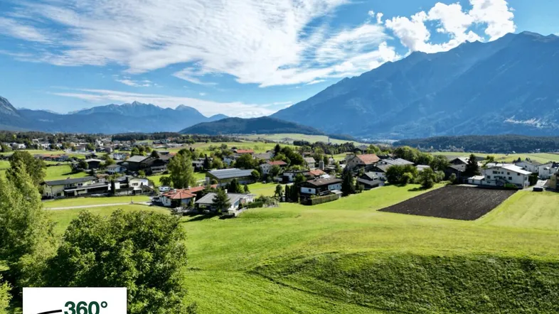 Weitläufige Luftaufnahme eines Dorfes in einem Tal mit majestätischen Bergen im Hintergrund und grünen Feldern.
