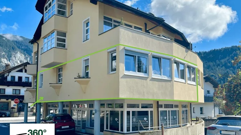 Mehrstöckiges Gebäude mit heller Fassade und großen Fenstern vor einer Bergkulisse.