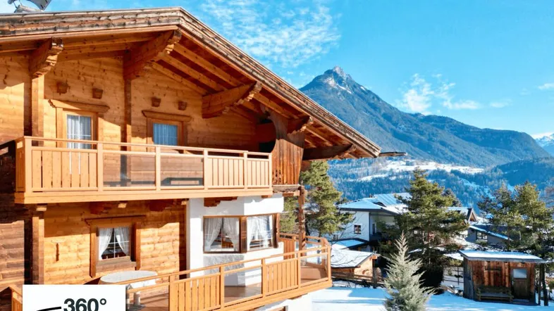 Charmantes Holzchalet mit mehreren Balkonen und beeindruckendem Bergblick in verschneiter Landschaft.