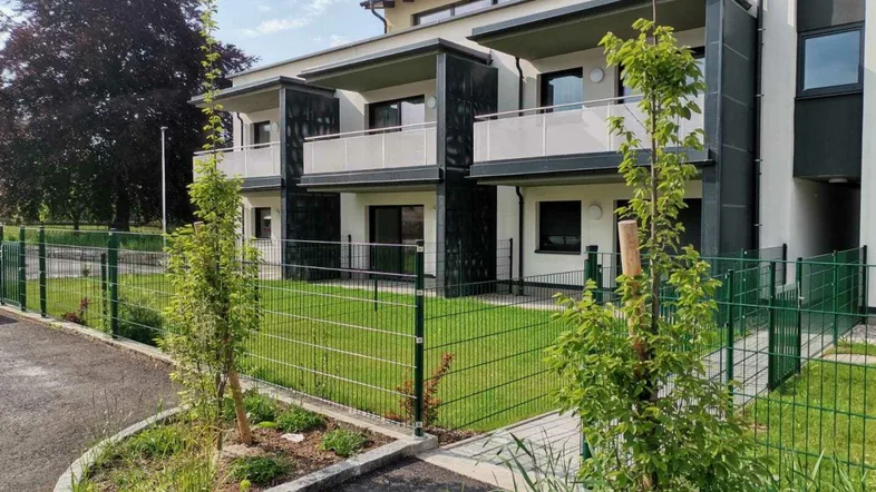 Modernes Mehrfamilienhaus mit Balkonen und gepflegter Grünfläche im Vordergrund.