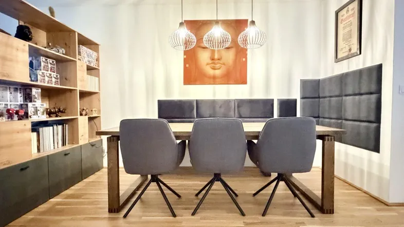 Moderner Essbereich mit Holztisch, bequemen Stühlen und einem dekorativen Wandbild, ergänzt durch ein Holzregal.