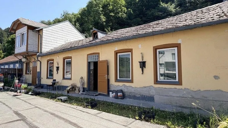 Gelbe Fassade eines älteren Gebäudes mit mehreren Fenstern und einem kleinen Vorplatz.