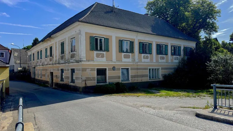 Altes, großes Gebäude mit traditioneller Architektur, grünen Fensterläden und einer verwitterten Fassade an einer Straßenecke.