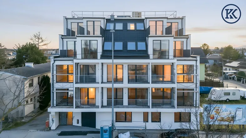 Modernes Mehrfamilienhaus mit mehreren Balkonen und großen Fenstern bei Sonnenuntergang.
