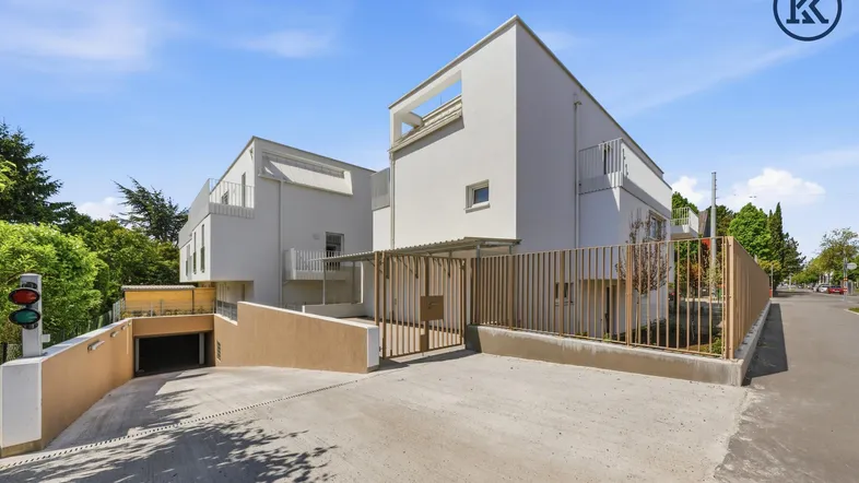 Moderne Wohnanlage mit weißer Fassade und Zufahrt zur Tiefgarage unter blauem Himmel.