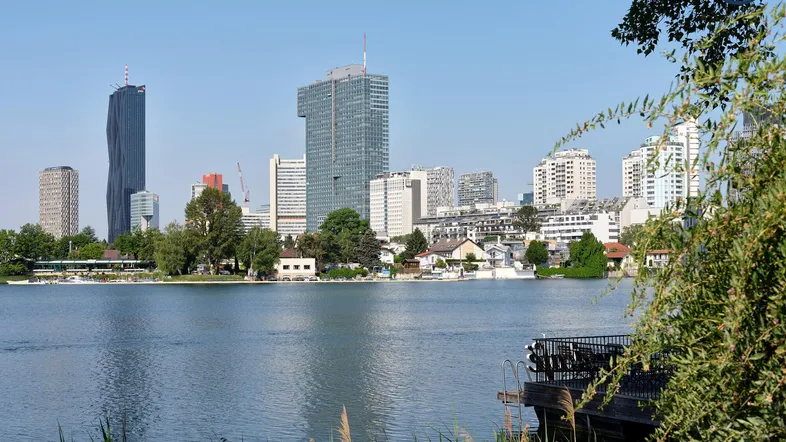 Panoramablick auf die Wiener Skyline mit modernen Hochhäusern und einem ruhigen See im Vordergrund.