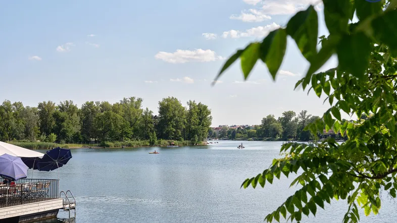 Seeufer mit schwimmender Terrasse und Blick auf die ruhige Wasseroberfläche unter blauem Himmel.