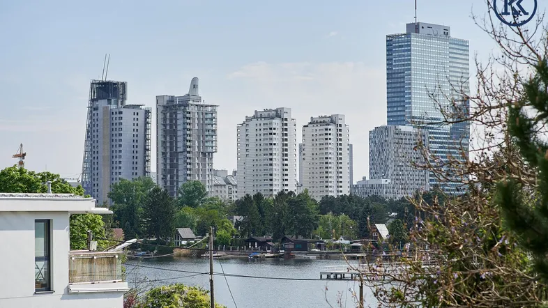 Panoramablick auf die Stadtlandschaft mit modernen Hochhäusern und einem ruhigen See im Vordergrund.