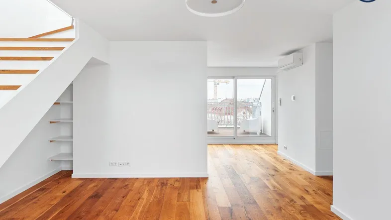 Helles Wohnzimmer mit Holzfußboden, Treppe und Zugang zu einem Balkon.