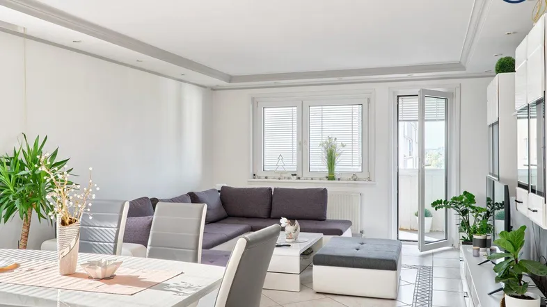 Helles Wohn- und Esszimmer mit modernem Sofa, Esstisch und Zugang zu einem kleinen Balkon.