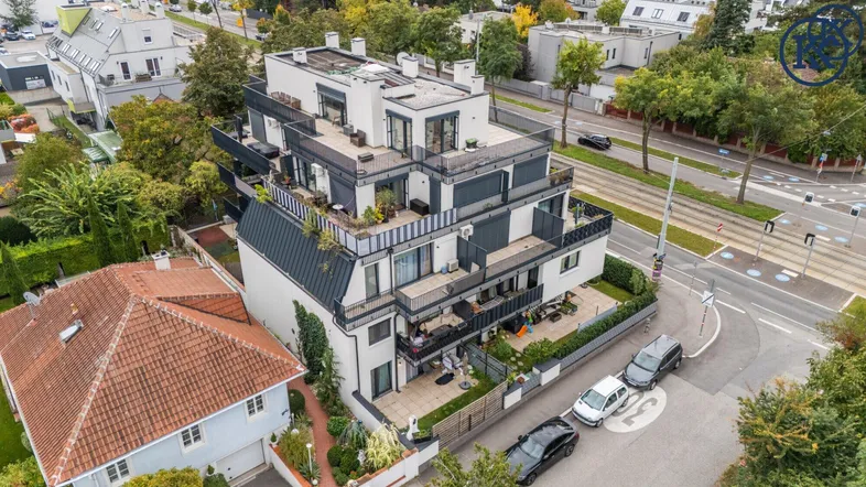 Luftaufnahme eines modernen Apartmentgebäudes mit mehreren Terrassen und Balkonen in grüner Umgebung.