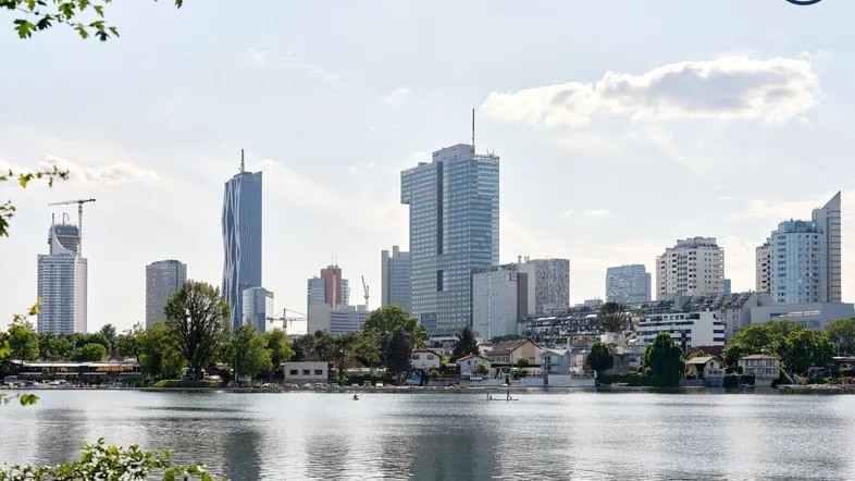 Stadtansicht mit modernen Hochhäusern am Ufer eines Sees unter bewölktem Himmel.