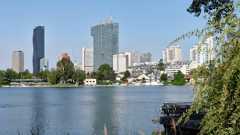 Stadtansicht mit See und moderner Skyline im Hintergrund unter blauem Himmel.