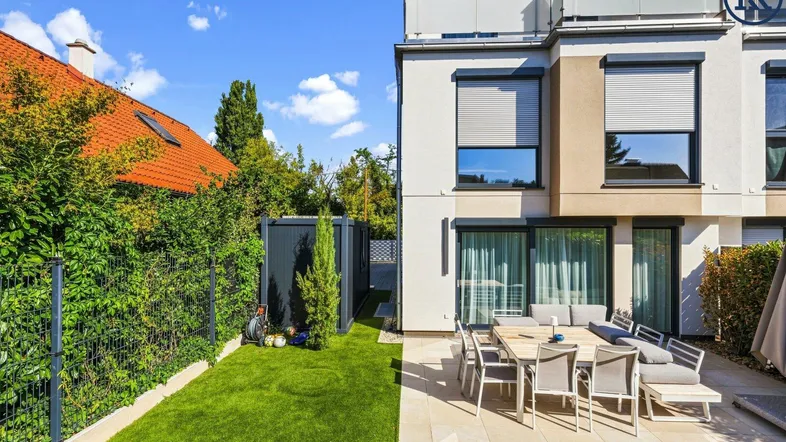 Moderne Terrasse mit Gartenmöbeln und angrenzendem Rasenbereich an einem sonnigen Tag.