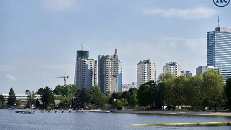 Panoramablick auf die moderne Stadtlandschaft mit hohen Gebäuden und einem ruhigen See im Vordergrund.