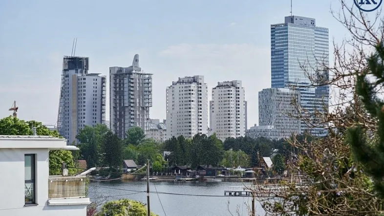 Panoramablick auf die Stadt mit modernen Hochhäusern und einem See im Vordergrund, umgeben von viel Grün.