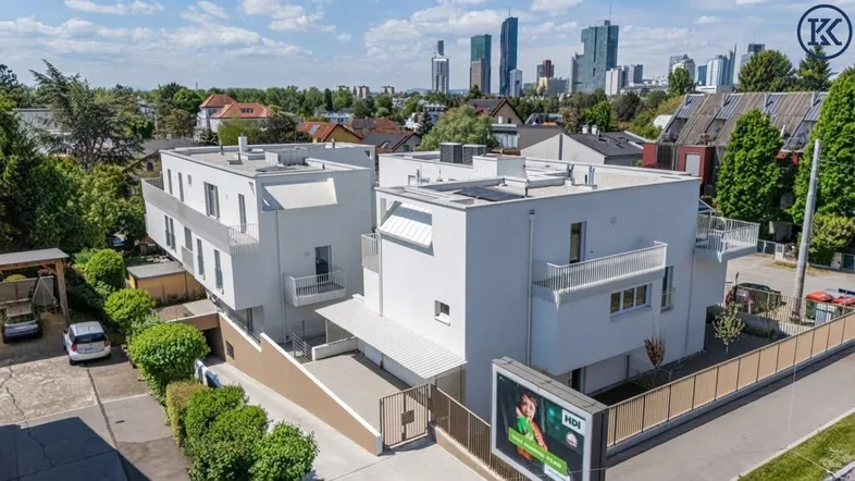 Moderne Wohngebäude mit Flachdächern und Balkonen, umgeben von Grünflächen und Stadtblick.
