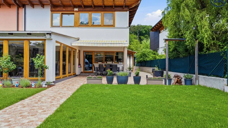 Großzügiger Gartenbereich mit Rasenfläche, gepflastertem Weg und überdachter Terrasse am Haus.
