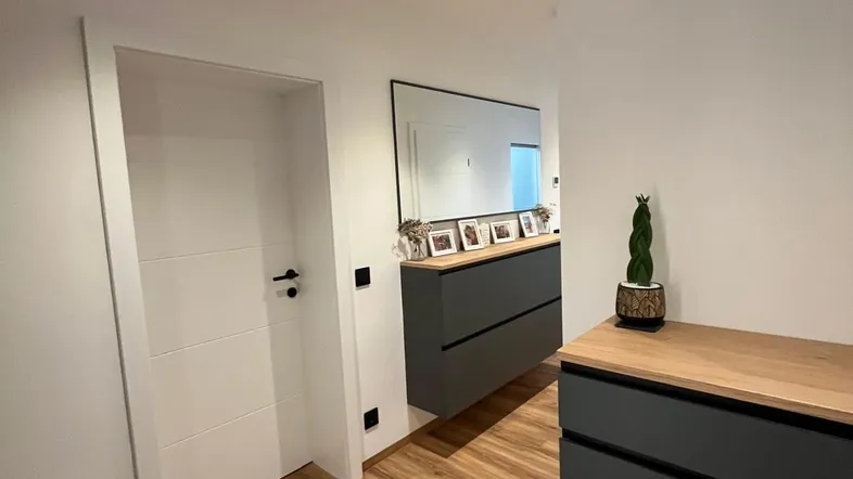 Moderner Flur mit Holzfußboden, weißer Tür und dunklen Möbeln mit Holzoberfläche.
