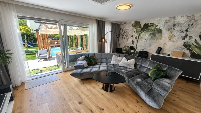 Helles Wohnzimmer mit großem Ecksofa, Holzboden und direktem Zugang zum Garten und Pool.