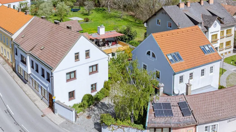 Luftaufnahme eines Wohngebiets mit mehreren Häusern und grüner Umgebung unter blauem Himmel.