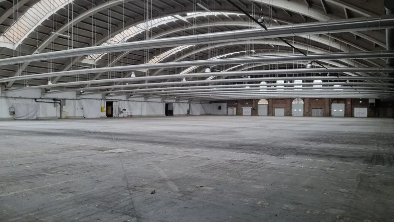Große, leere Industriehalle mit gewölbter Decke und Oberlichtern, ideal für Lager oder Veranstaltungen.